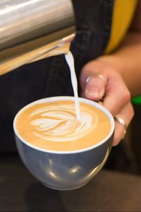 Steamed milk is poured into a coffee cup to make a latte,  and making a pattern on top. At Urban Angel cafe Edinburgh