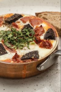 A copper skillet with fritatta with black pudding and chorizo. In the background a slice of toasted sourdough. A brunch dish at Urban Angel cafe, central Edinburgh